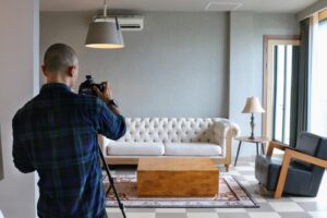 Photographer taking pictures of a modern living room with a sofa, coffee table, and armchair.