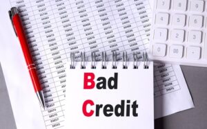 The image shows a notepad with the words "Bad Credit" in bold next to a red pen, calculator, and financial documents, symbolizing How to rent a House with Bad credit.