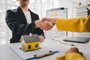 Two people shaking hands over a desk, with a small model of a house on a clipboard, symbolizing how to show proof of income without paystubs.
