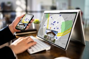 A person using a laptop and smartphone to view a real estate map and property listing.