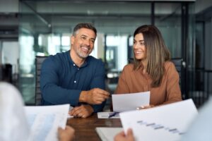 A happy couple sits at an office table with paperwork discussing what is included in property management fees.