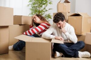 A tired couple sitting among moving boxes, appearing exhausted as they find out What Happens If You Don't Pay Rent?