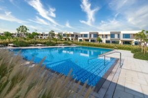An outdoor swimming pool with lounge chairs, surrounded by greenery and modern residential buildings under a clear sky.